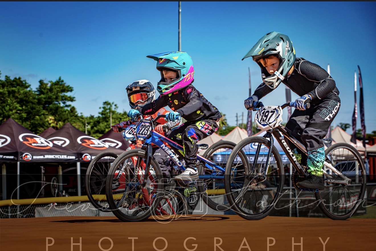 Sullivan Cagle launching from the BMX starting gate beside two riders