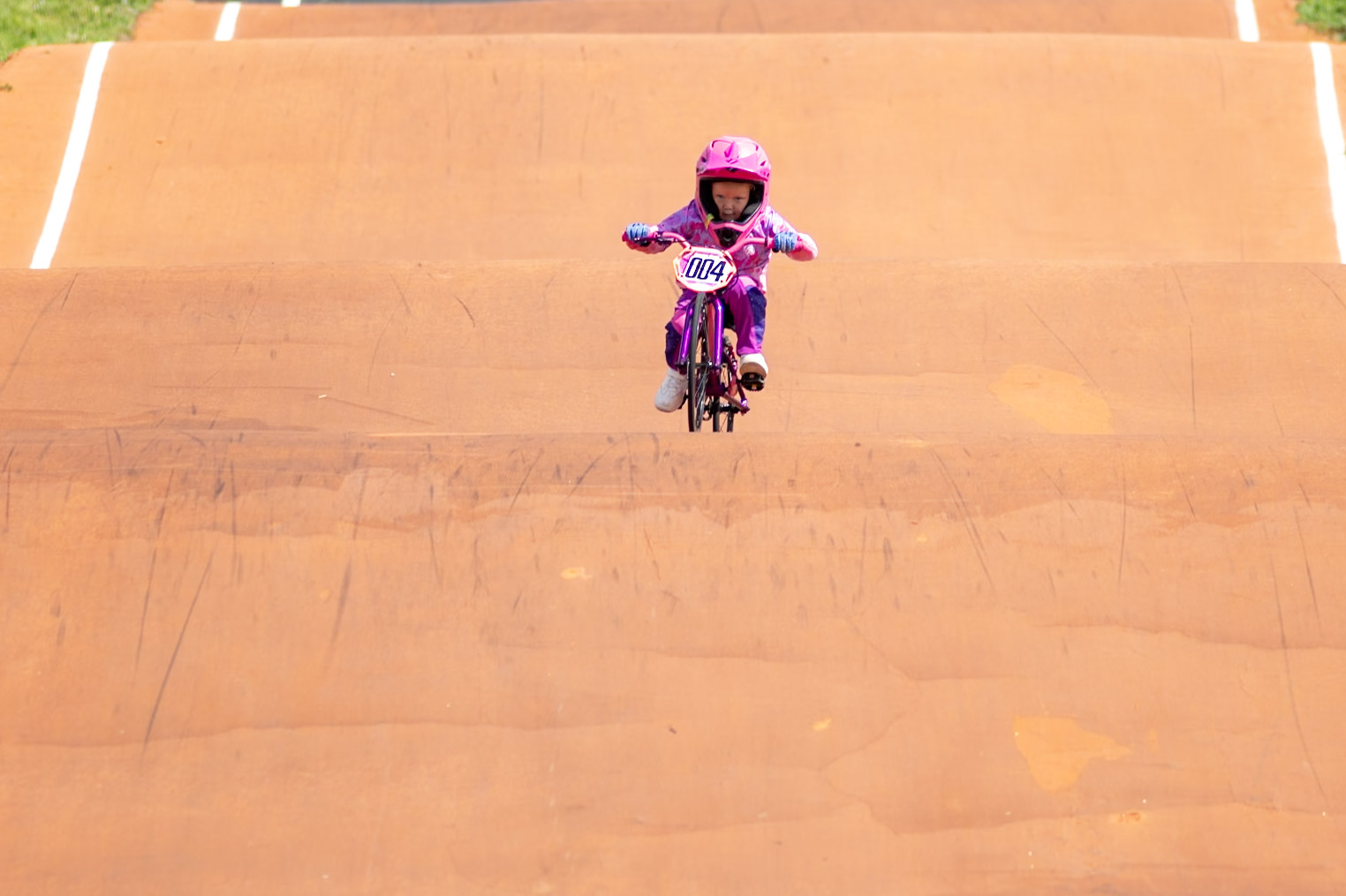 Summer Cagle racing number 004 over the orange BMX track rollers